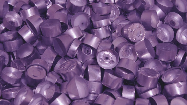 A still image from a video artwork by Michelle Hall. The image is a close-up of hundreds of candle tealights. The crumpled metal casings of the tealights shows that the candles have already been burned. A light purple colour is used as a filter over the whole image.
