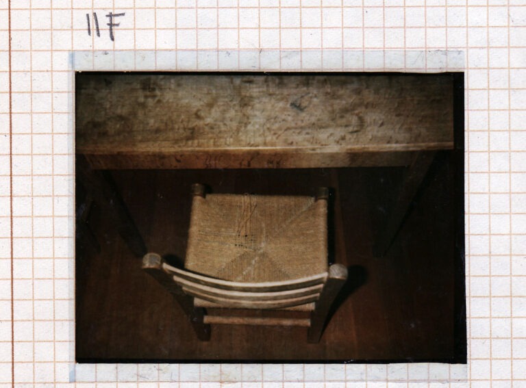 An image taken looking down on an old wooden kitchen chair with woven seat, placed beside a wooden table