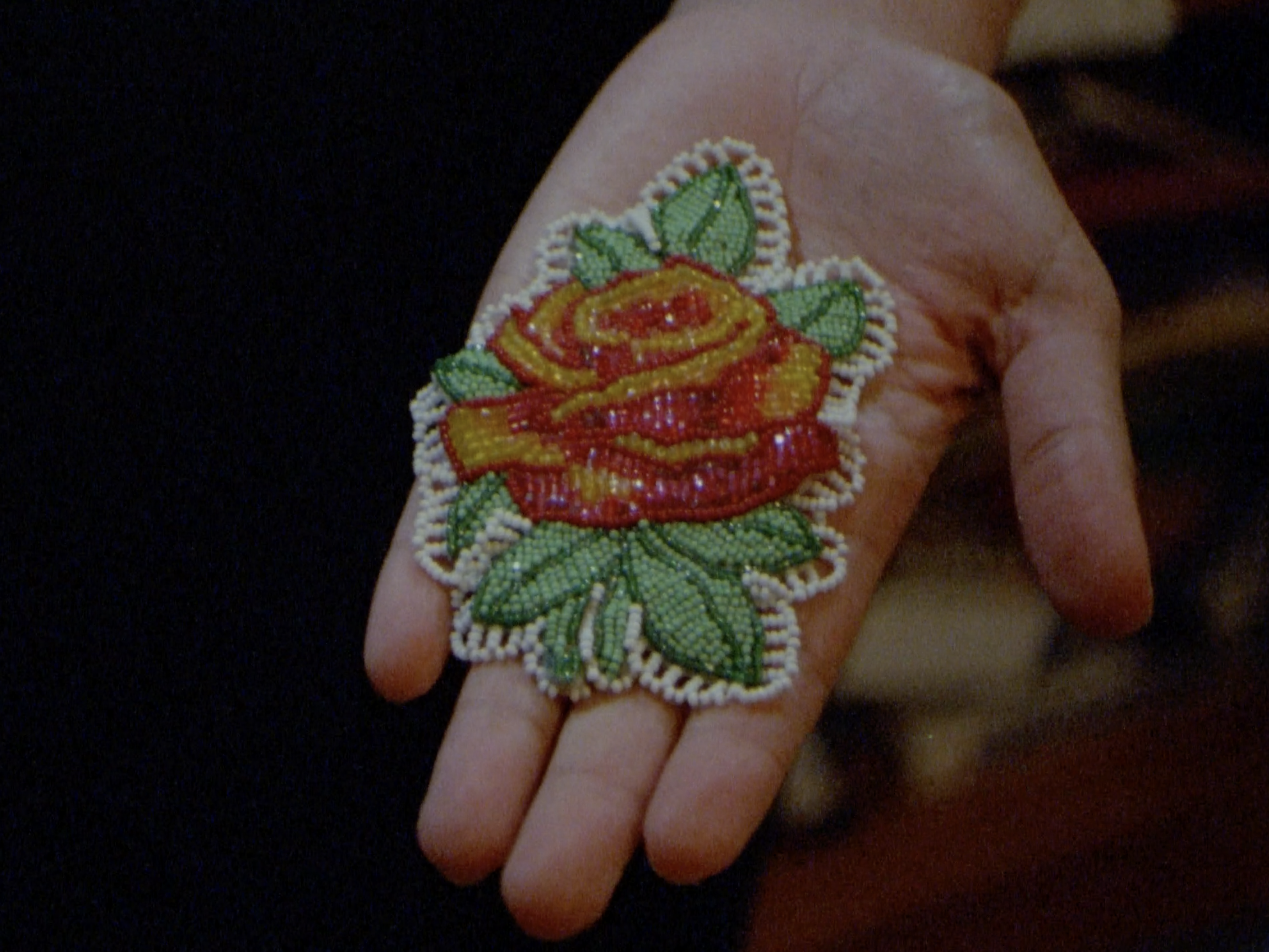 In the palm of a person with light skin is an extremely detailed red rose created entirely from tiny beads
