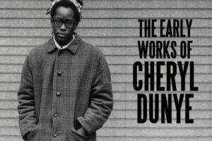 Black and white image of Cheryl Dunye, a Black person standing in front of a wall. Cheryl is wearing a long buttoned-up coat, with a white shirt collar showing, a hairband, and glasses. To the left of Cheryl is large black text in all capitals which reads THE EARLY WORKS OF CHERYL DUNYE.