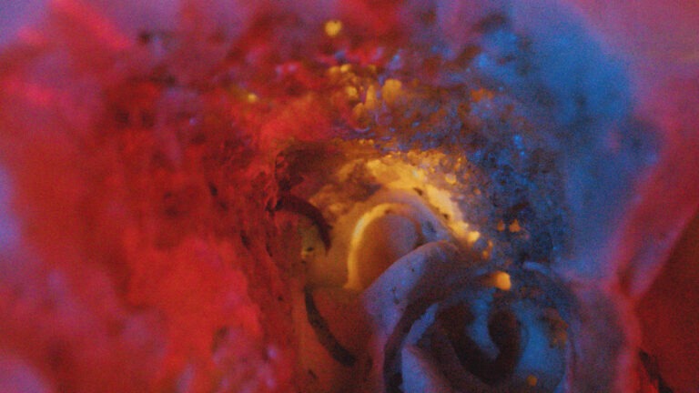 An abstract image mostly compiled of vivid colour and texture. On the left is mostly red, which moves into a glowing yellow/amber colour and then blue. It appears as though the viewer might be looking into a hole or void of some kind.