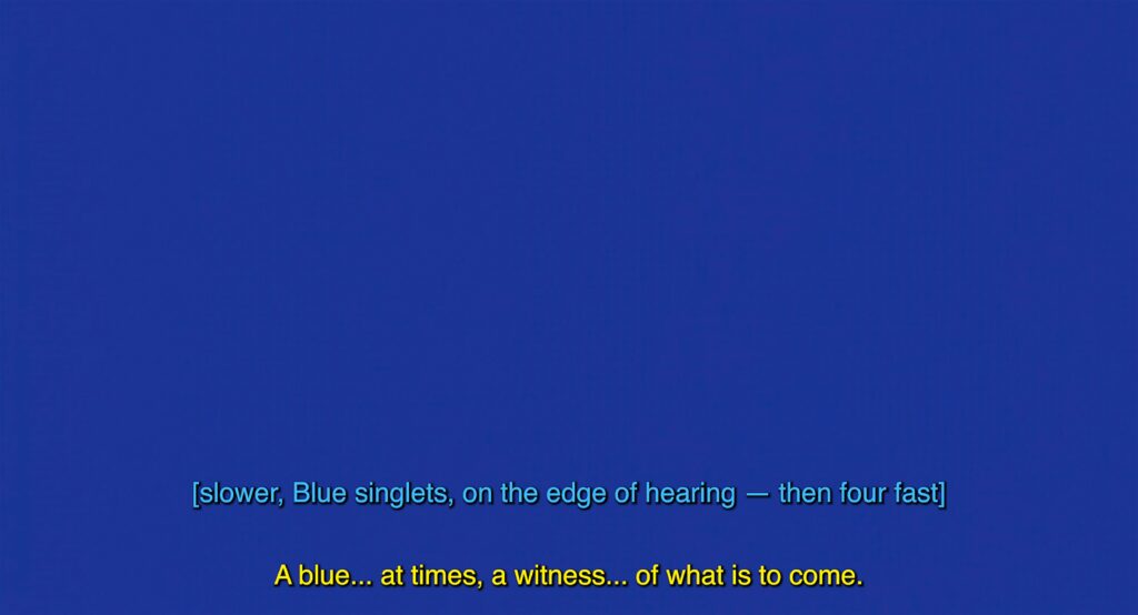 A single shot of saturated blue colour fills the image. This rich, vivid blue colour is called International Klein Blue, named after the French artist Yves Klein who mixed the colour. This colour is a variation or shade of Ultramarine; which was made by grinding lapis lazuli or a synthetic equivalent called French Ultramarine. The image is captioned twice, the top line reads: (slower, Blue singlets, on the edge of hearing - then four fast) this text is displayed in a turquoise colour. The caption underneath reads: A blue...at times, a witness...of what is to come. This text is displayed in a bright yellow colour.